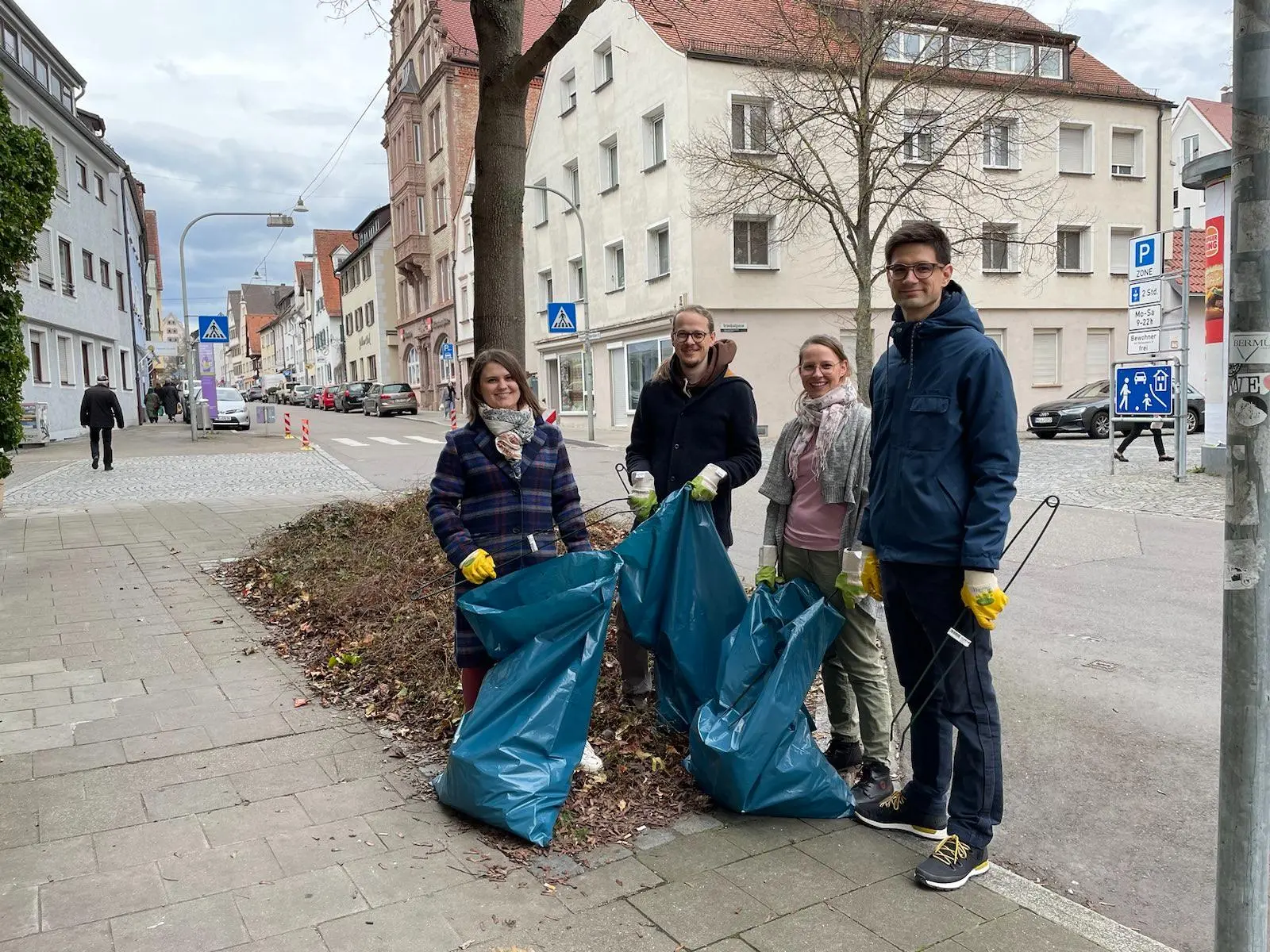 Mareike und Dominik Burgdörfer, Franziska Riesenberg und Jonas Meer stehen lächelnd, mit Müllsäcken und Greifzangen, vor einem Baum.